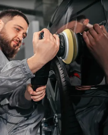 A technician machine polishing a black car body panel in the shop.